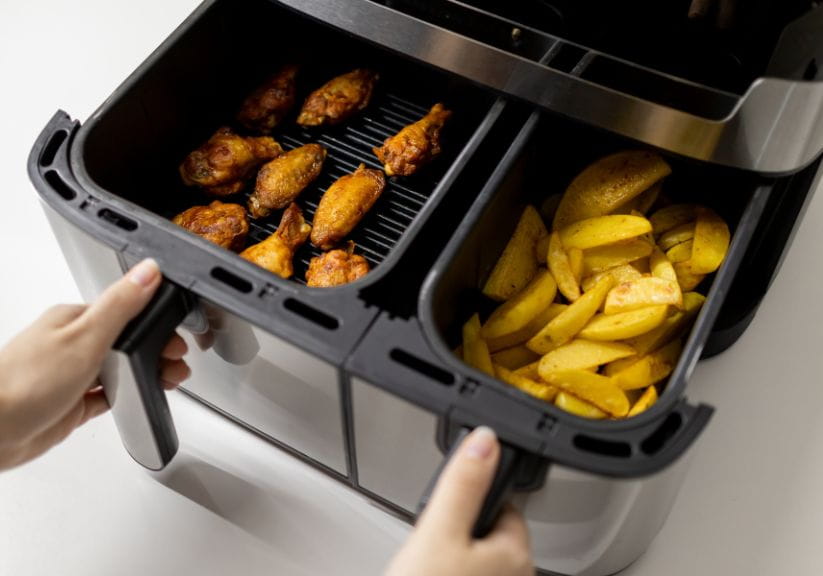 Someone taking out two baskets from an air fryer