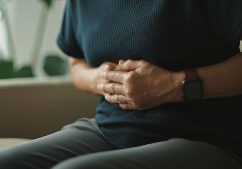 A woman clasps at her stomach while sitting down