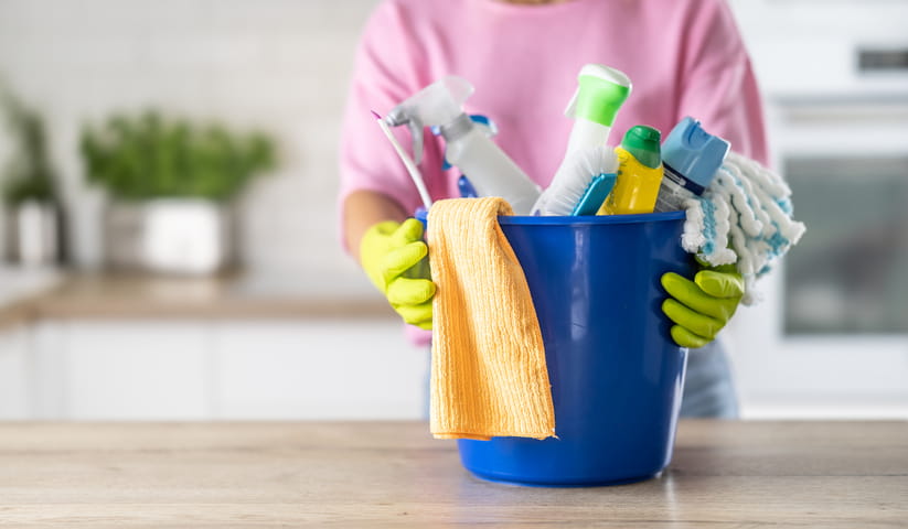 A woman with a bucket load of cleaning products on a kitchen work surface