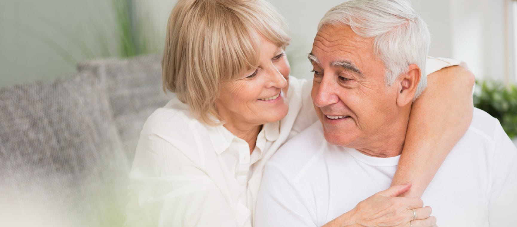 Older couple wearing white and cuddling on sofa