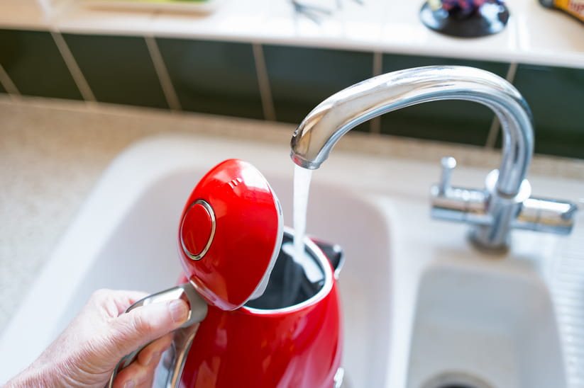 A red kettle being filled up with water in a sink