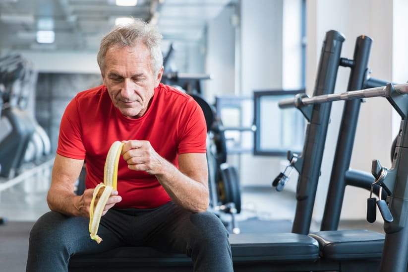 Mature man eating banana at the gym