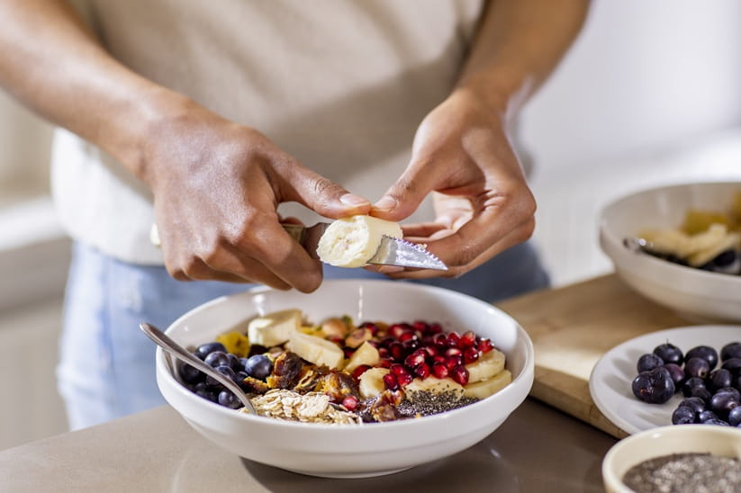Close up of someone cutting a banana for a healthy breakfast of fruits and yogurt
