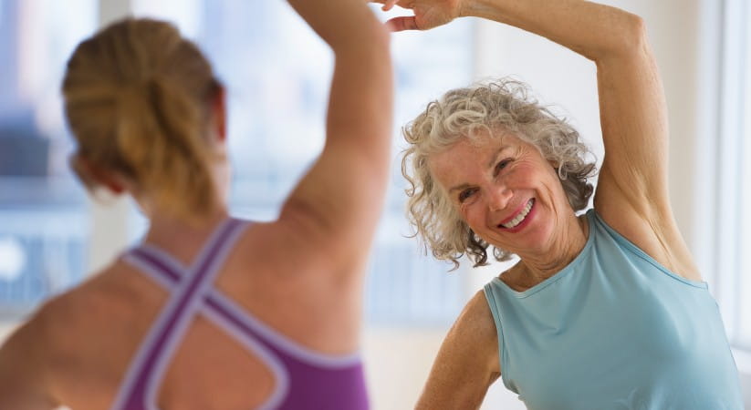 Older woman smiling while exercising with another woman