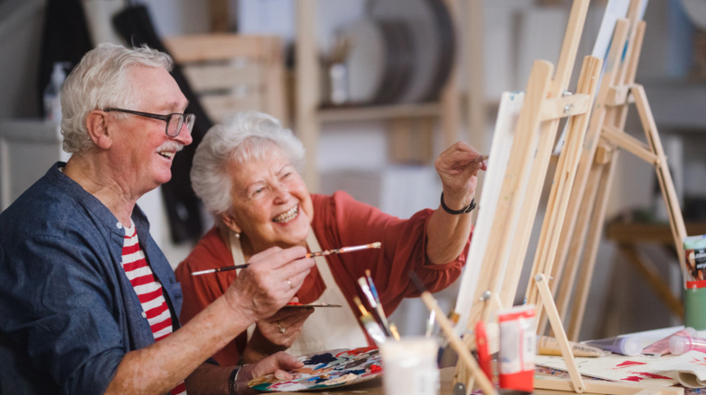 An older man and woman enjoying painting together on an easel