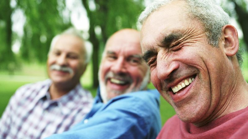 three older men sat in a park laughing together