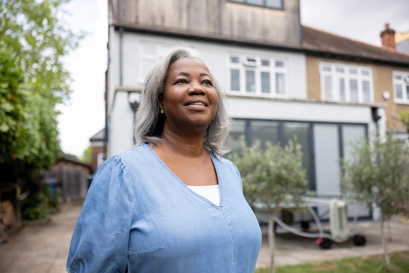 A woman smiles as she stands in front of a large suburban house