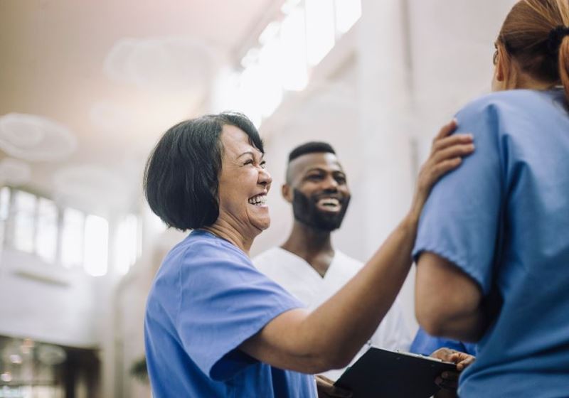 Side view of happy senior female doctor with hand on shoulder of colleague at hospital