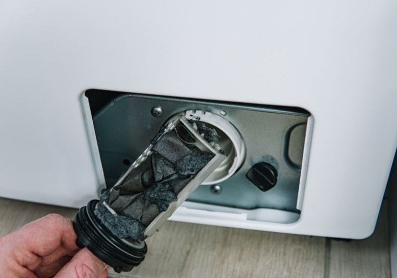 Someone removing a clogged filter from a washing machine