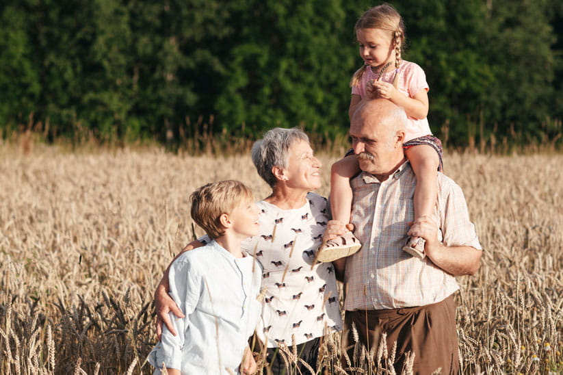 Two smiling elderly people with two grandchildren in a field of oats