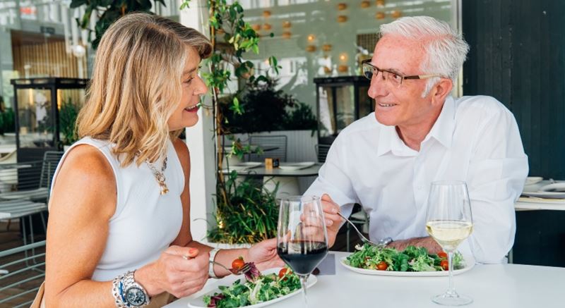 Older couple in white looking at each other as they eat a salad in a restaurant