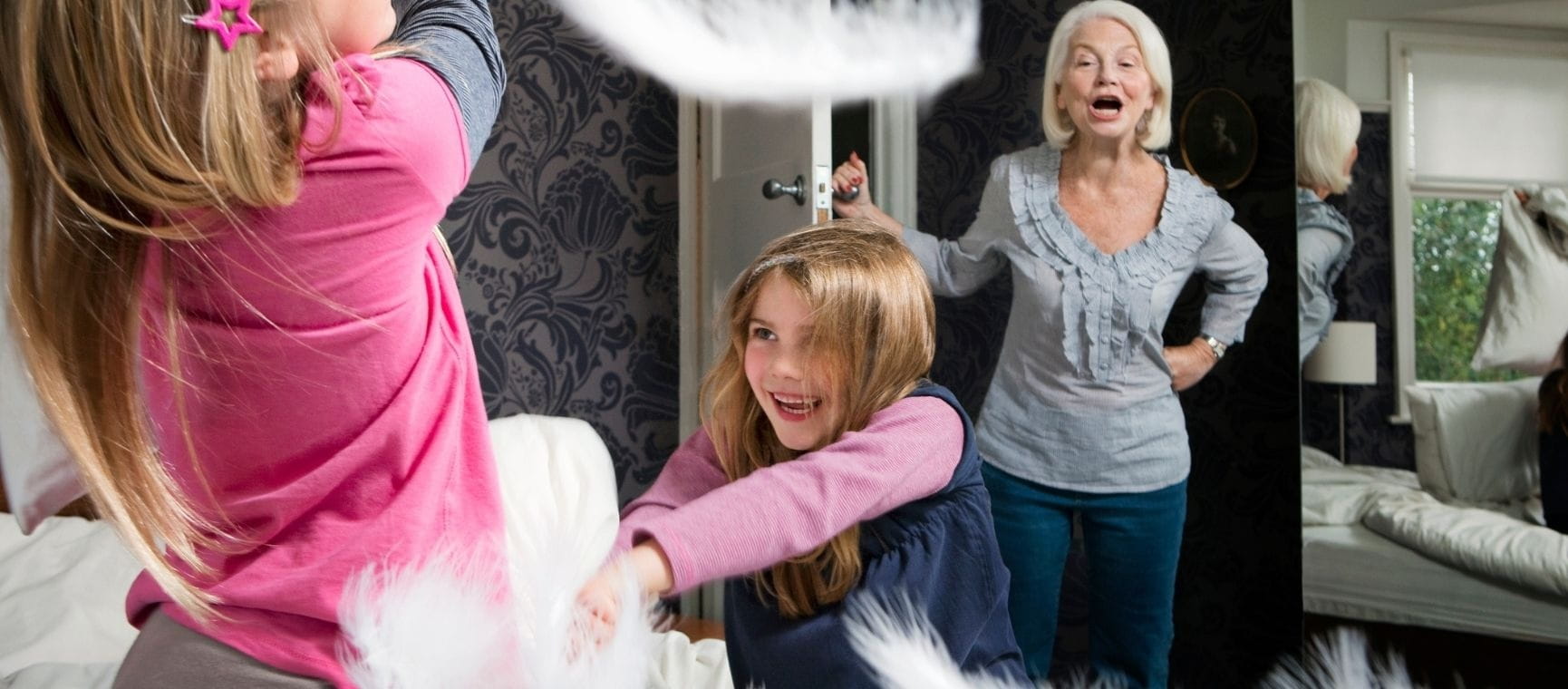 two young girls playing with pillows being told off by their grandmother