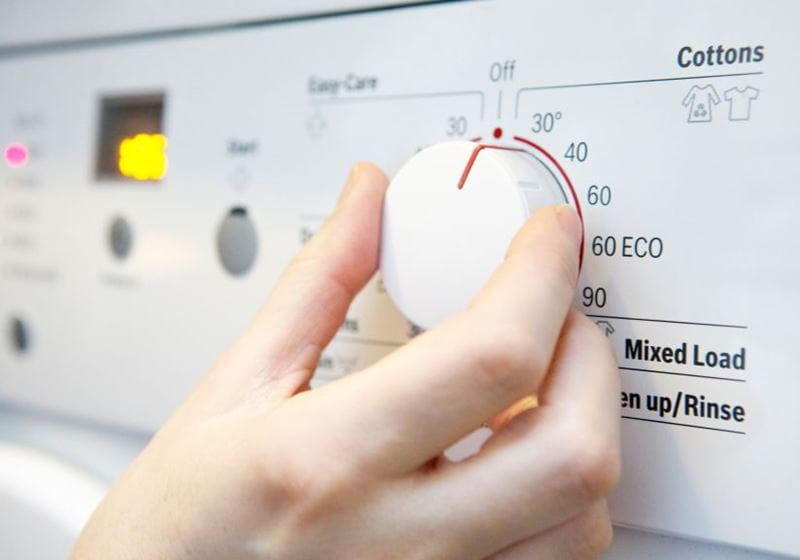 Someone setting the dial on a washing machine to 30