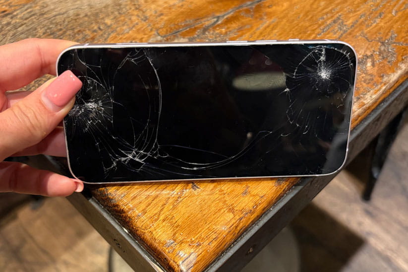 Hand holding a mobile phone with a cracked screen