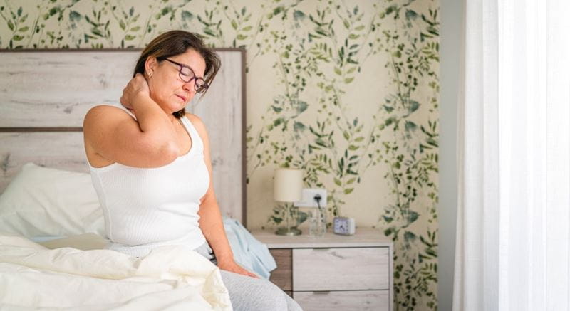 Woman in white looking unhappy as she sits on her bed