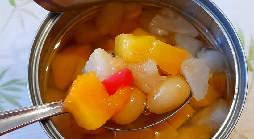 Close up of an open tin of fruit with a spoon in it