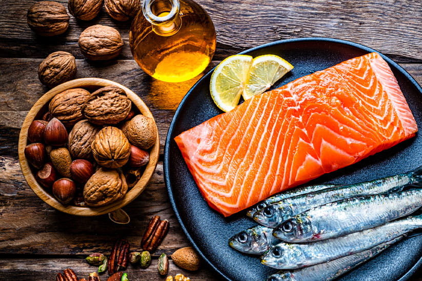 A plate with salmon and mackerel next to a bowl of nuts on a wooden table