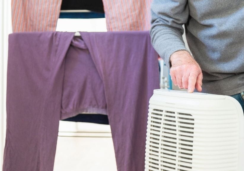 A man switching on a dehumidifier next to drying clothes