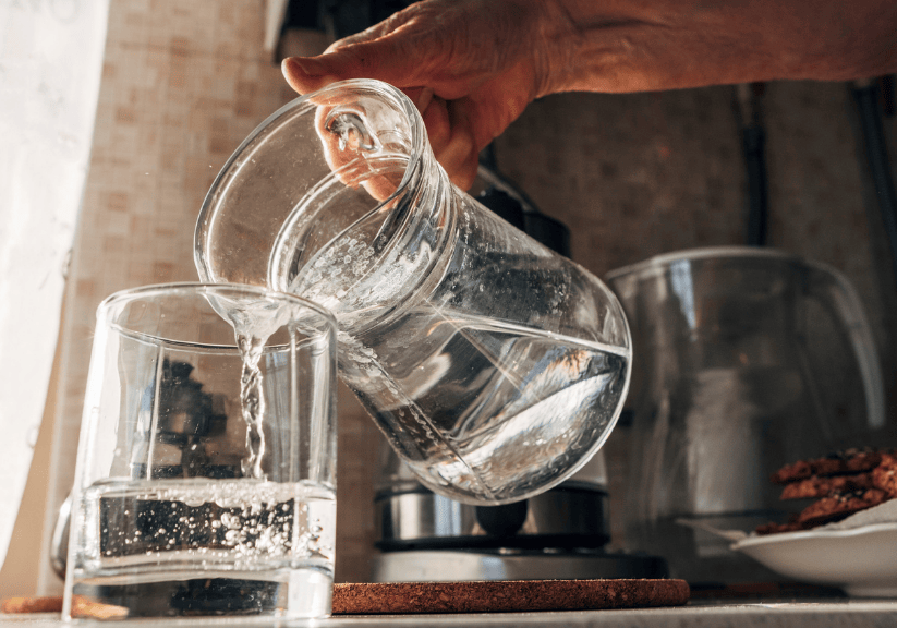 An older person pouring a glass of water from a clear jug