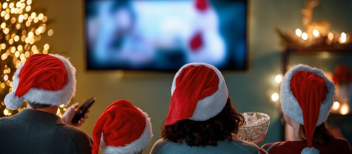 A family wearing Santa hats watching television at Christmas