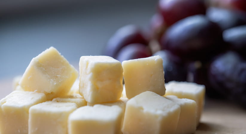 Chunks of Cheddar cheese with red grapes in the background