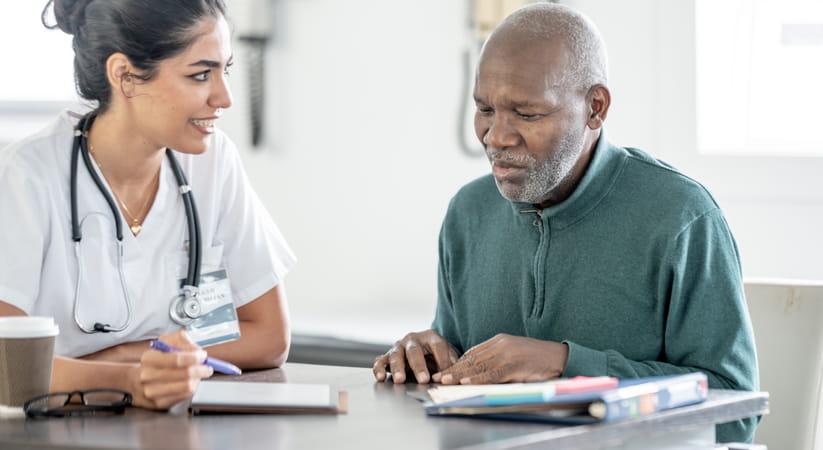 Female doctor in a white gown talking to an older man in a green shirt