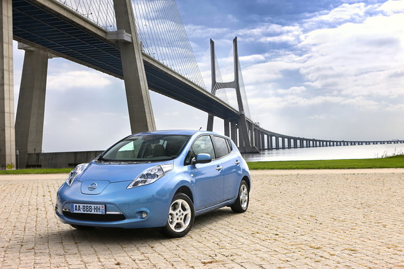 A light blue Nissan Leaf next to a bridge