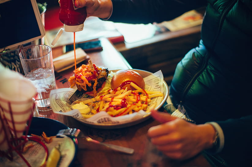 Burger and chips being covered in ketchup