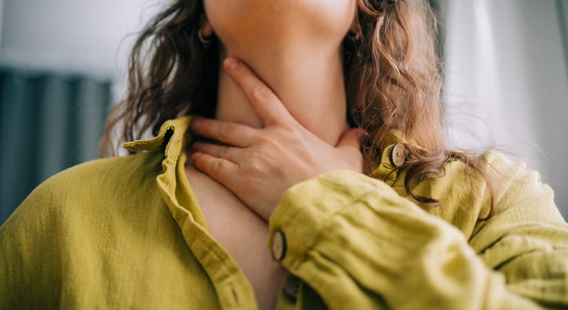 Close up of a woman in a yellow top holding her throat with her left hand