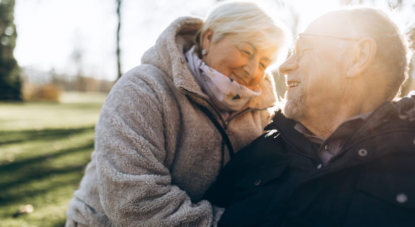 An older man and woman in coats joke about while bathed in golden afternoon sunshine