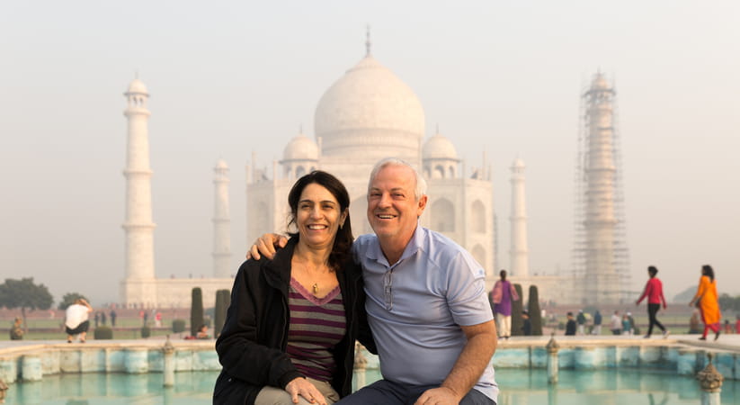 An older couple pose together in front of the Taj Mahal in India