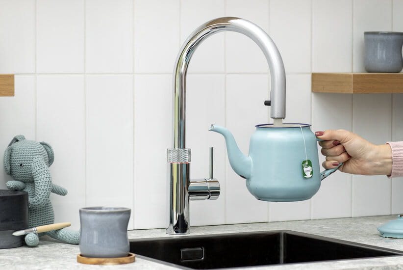 Close up of hand filling a blue kettle under a hot water tap