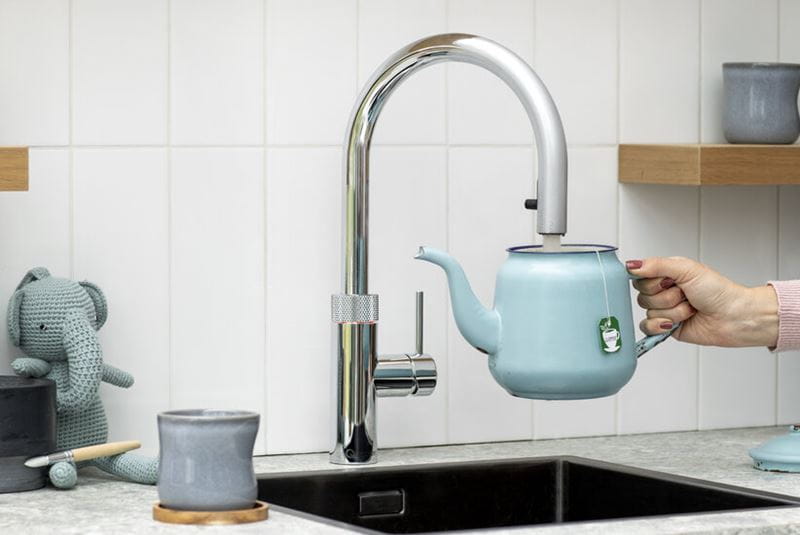 Close up of hand filling a blue kettle under a hot water tap