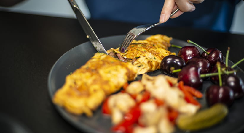 Close up of a person eating a plate of frittata with a knife and fork