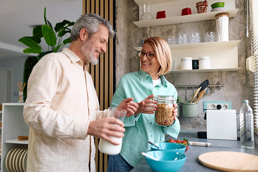 Older adult couple happily preparing a healthy breakfast with cereal and milk in bright kitchen