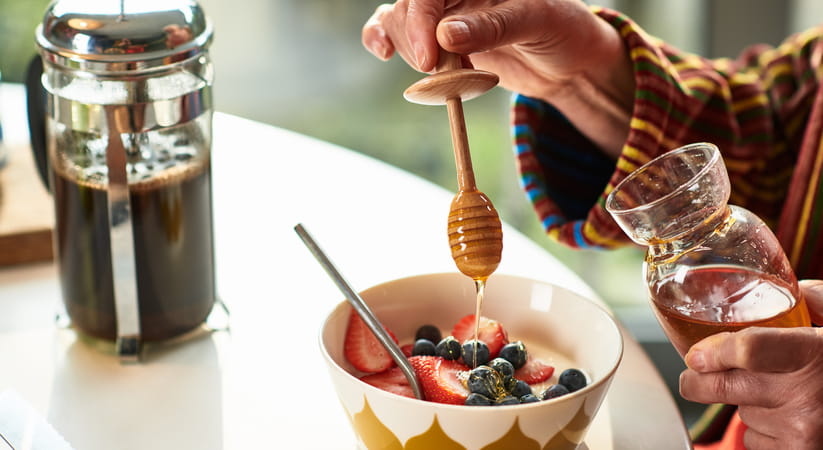 Close up of a woman pouring honey into a bowl of porridge and fruit