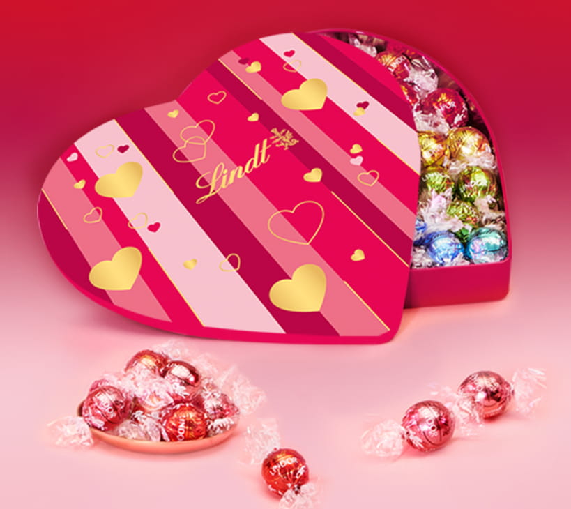 Open box of Lindor heart chocolates against a pink background