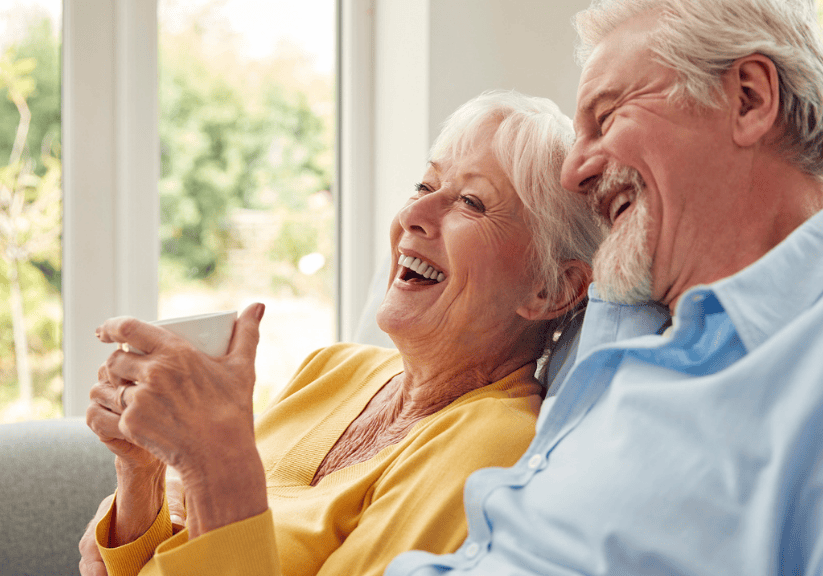 A happy older couple drinking tea and laughing on a sofa