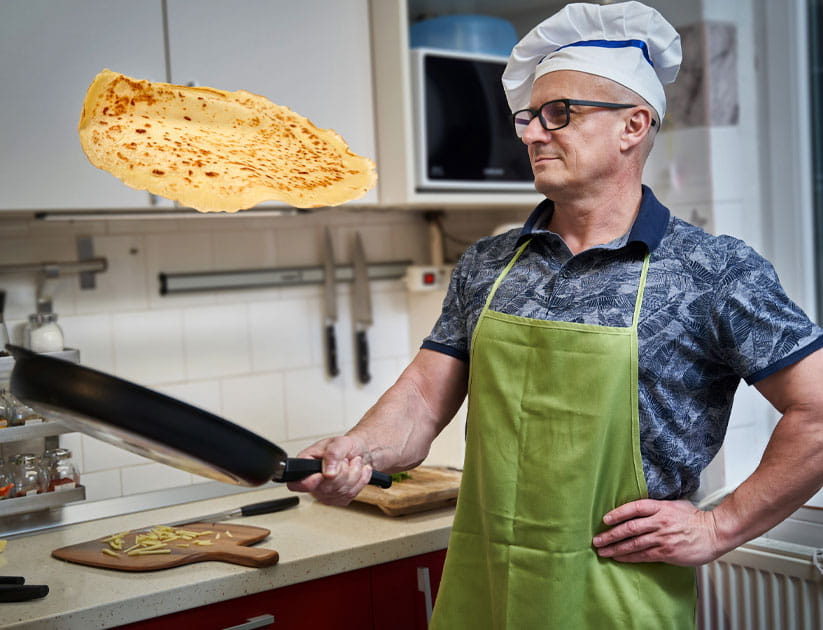 Man cooking at home, flipping a large pancake with skill in a large pan