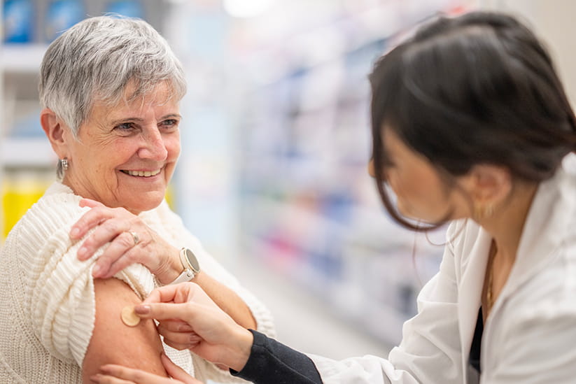 A Pharmacist applying a small adhesive bandage to an older woman following a flu vaccination