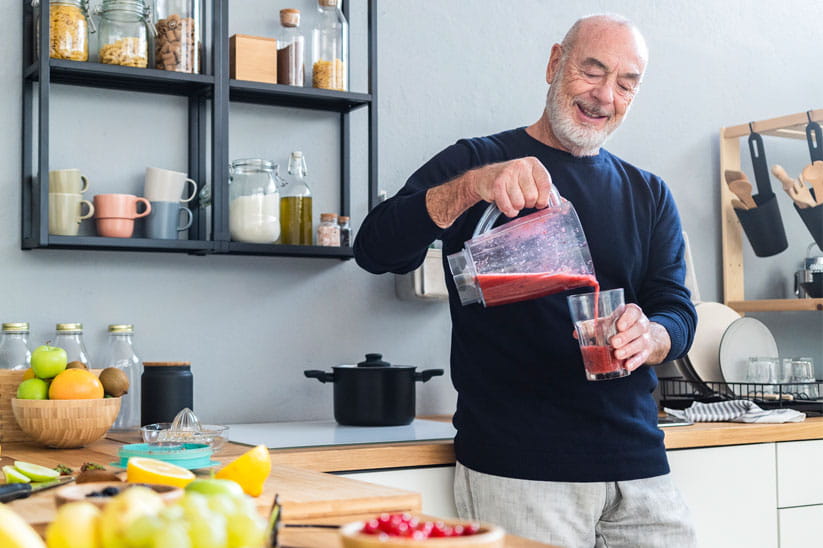Senior man in a kitchen pouring a smoothie into a glass from a blender