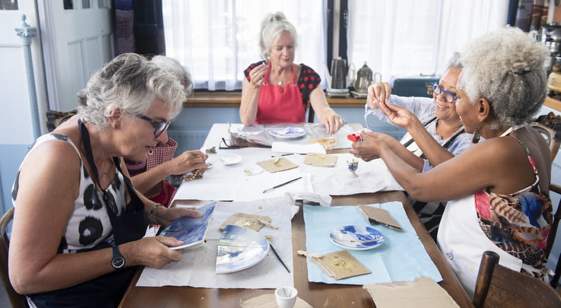 A group of older women sit round a table crafting