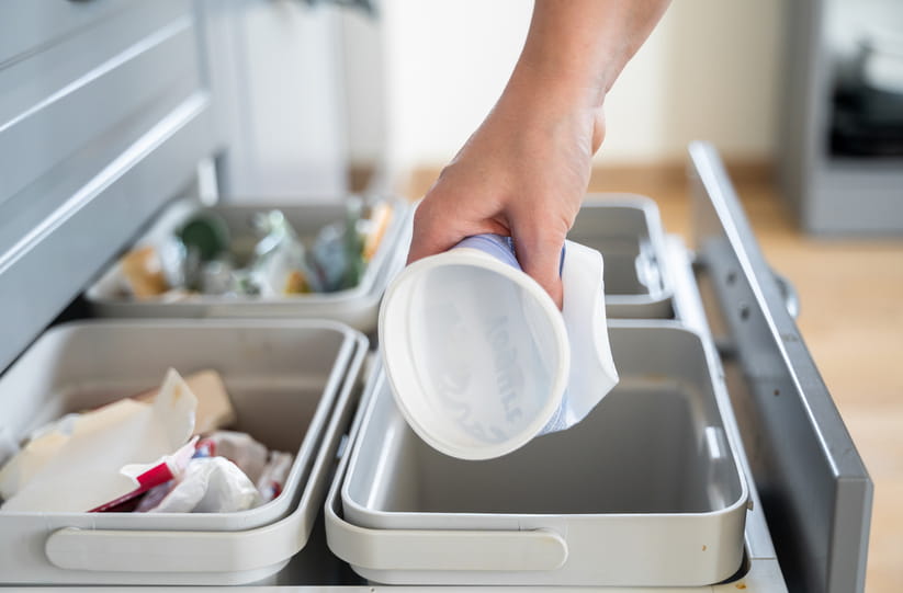 A close up of a hand putting an empty yoghurt pot in the recycling bin