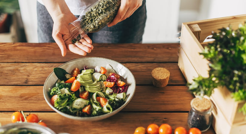 Close up of a female hand pouring some seeds from a jar to add to a bowl of salad
