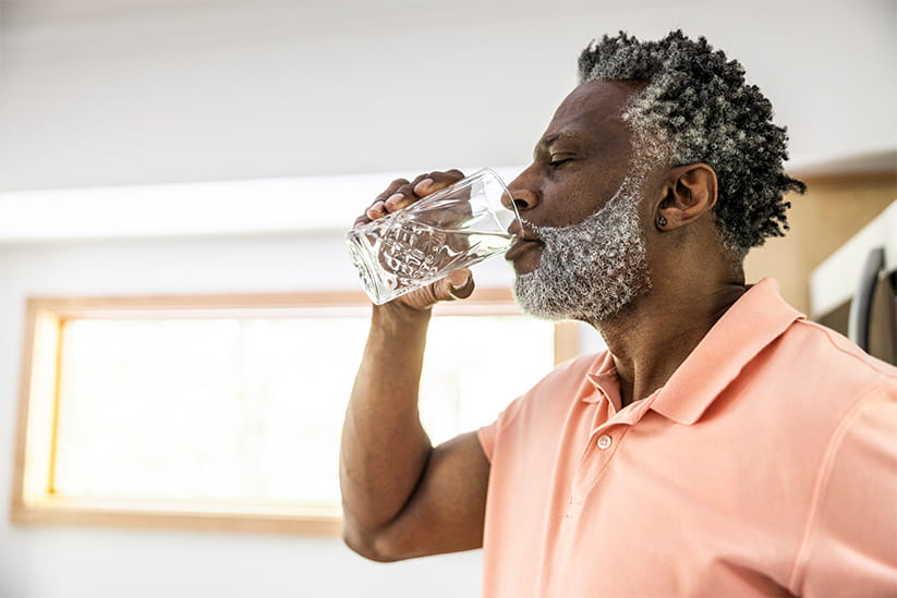An older man in a salmon coloured polo shirt drinks a glass of water