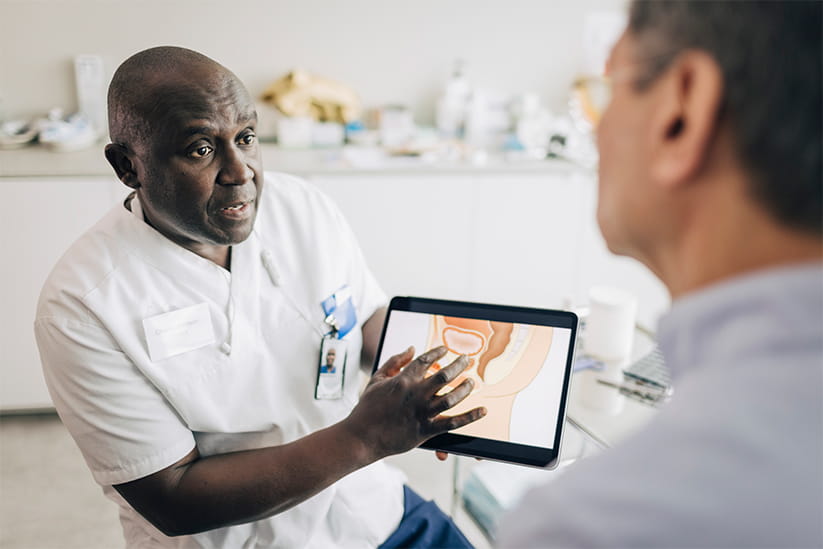 A doctor shows a diagram of the prostate area to another older man during a consultation 
