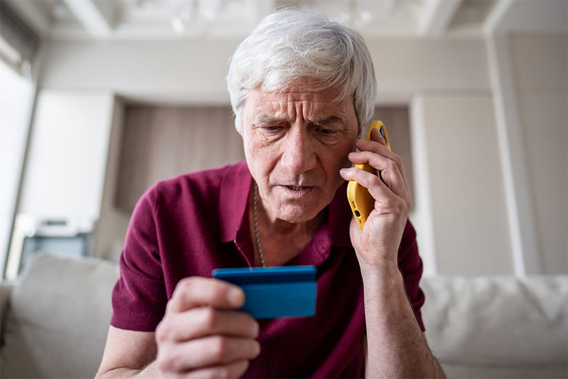 An older man looking at his bank card whilst on the phone, and looking worried