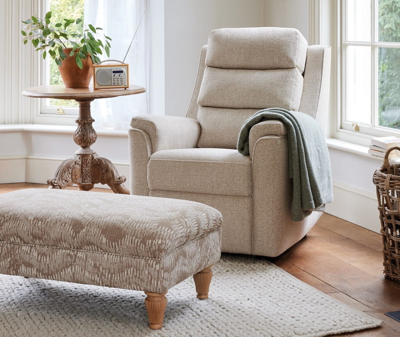 A cream coloured HSL Bramham armchair in a lounge with a footrest in front of it and a plant to its right