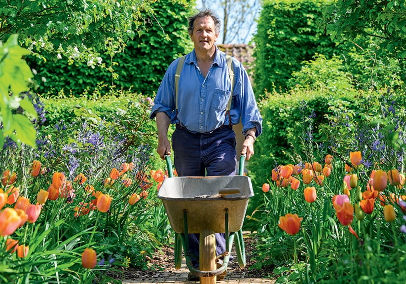 Monty Don pushes a wheelbarrow through a flower garden