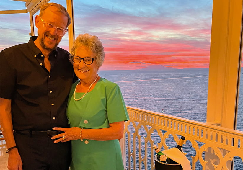 Barry Mays and Pat Swain pose together inside a cruise ship with the sea in the background
